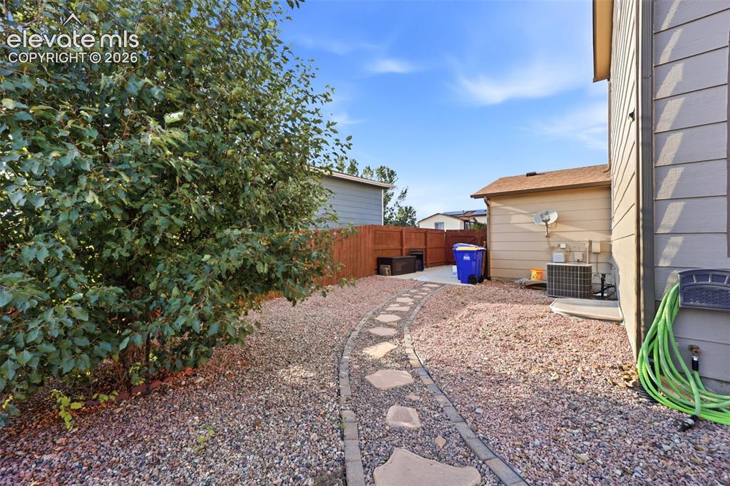 Image 34 of 40: Landscaped yard with a stone paver pathway, gravel ground cover, and mature