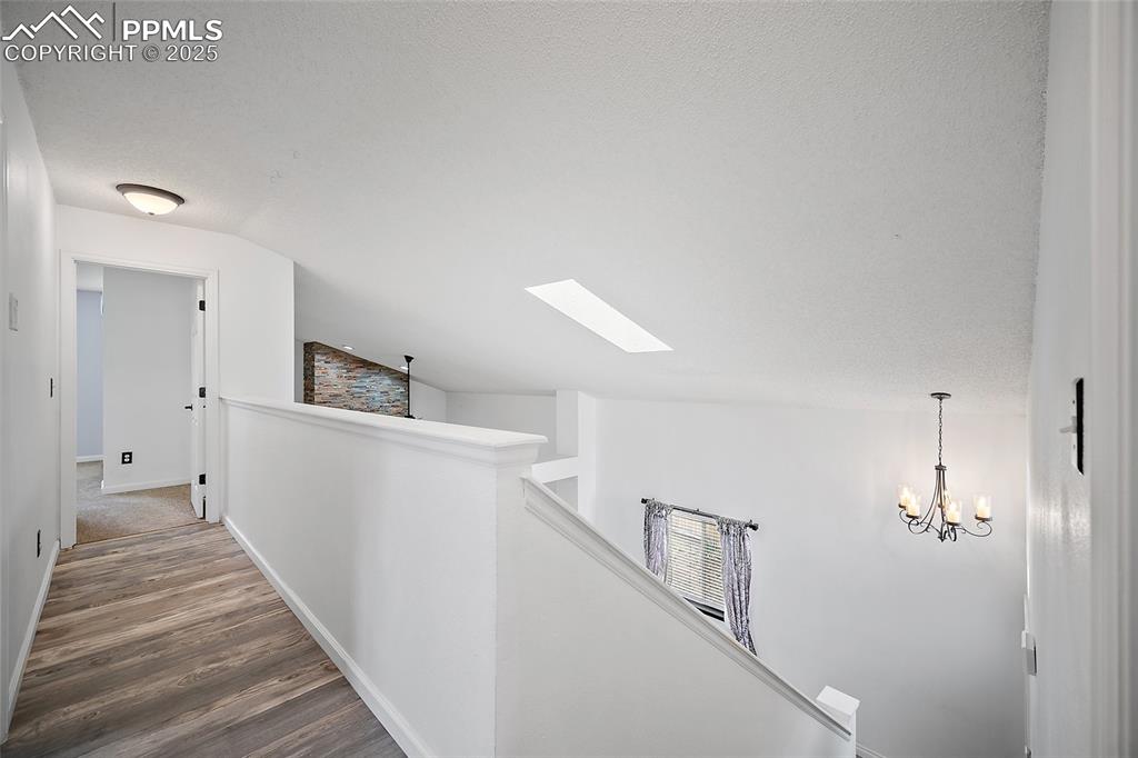 Image 27 of 50: Hallway featuring a skylight, an upstairs landing, dark wood-style flooring