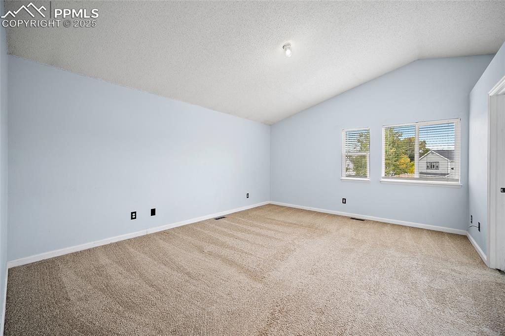 Image 28 of 50: Unfurnished room with vaulted ceiling, a textured ceiling, and light colore