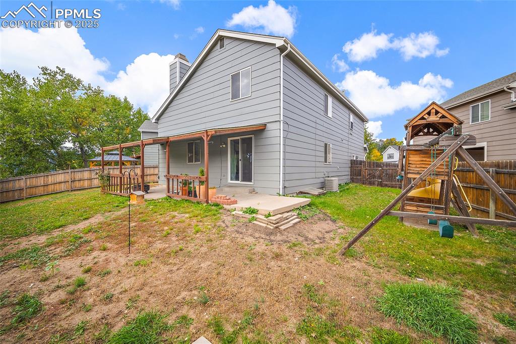 Image 47 of 50: Back of house featuring a fenced backyard, a playground, a chimney, and a p
