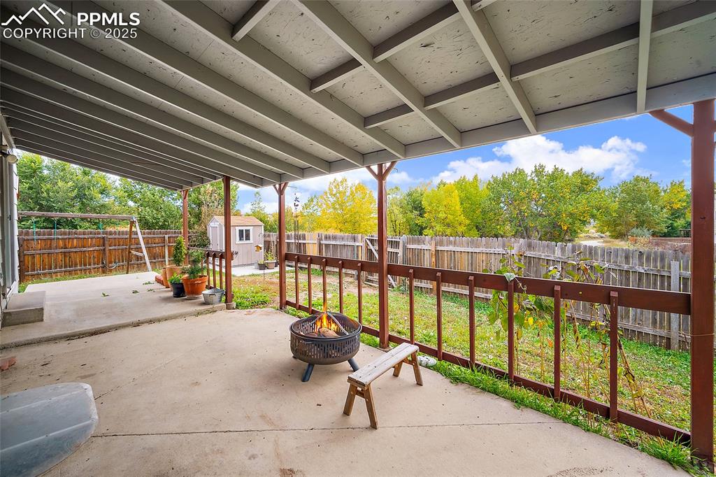 Image 48 of 50: Fenced backyard with a shed, a patio area, and a fire pit