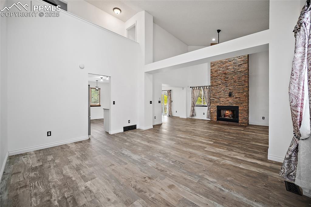 Image 8 of 50: Unfurnished living room with a fireplace, wood finished floors, and high va