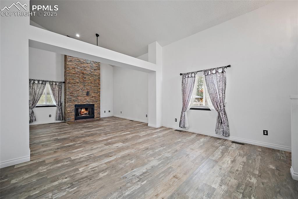 Image 9 of 50: Unfurnished living room with a stone fireplace, light wood-type flooring, a