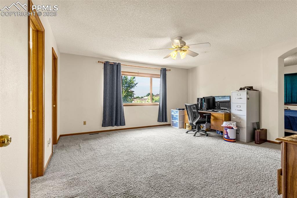 Image 10 of 33: Carpeted home office with a ceiling fan, a textured ceiling, and arched wal