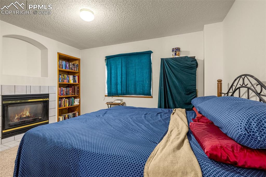 Image 15 of 33: Bedroom with a tiled fireplace and a textured ceiling