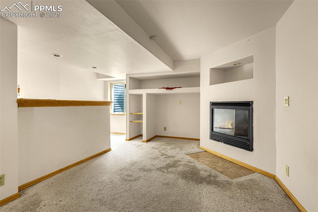 Image 21 of 33: Unfurnished living room with carpet flooring and a multi sided fireplace