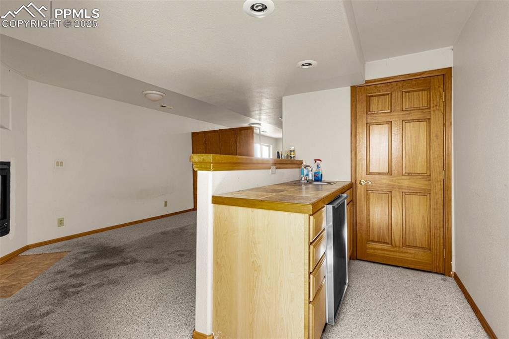 Image 22 of 33: Kitchen featuring light colored carpet, tile counters, and a peninsula