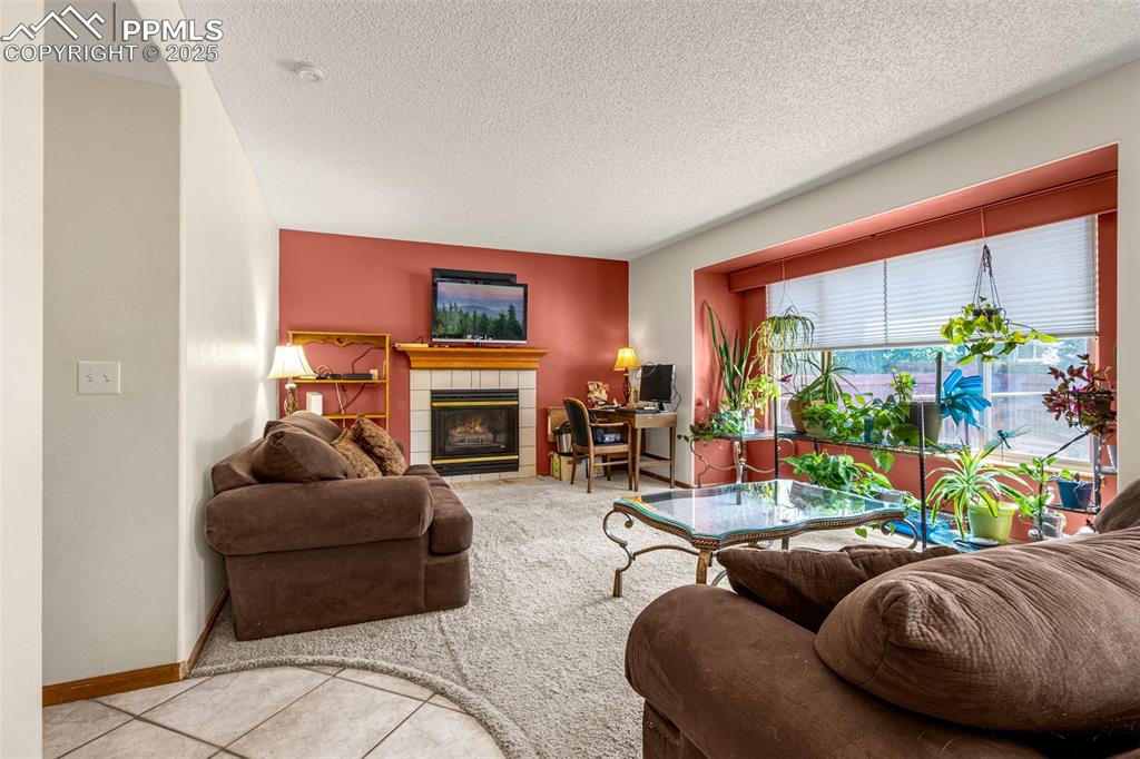 Image 5 of 33: Tiled living room featuring carpet, a tile fireplace, and a textured ceilin