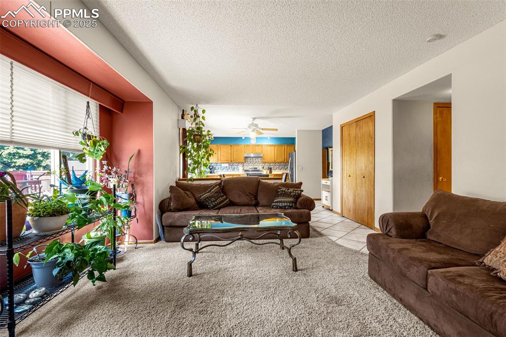 Image 6 of 33: Living area with a textured ceiling, light colored carpet, ceiling fan, and