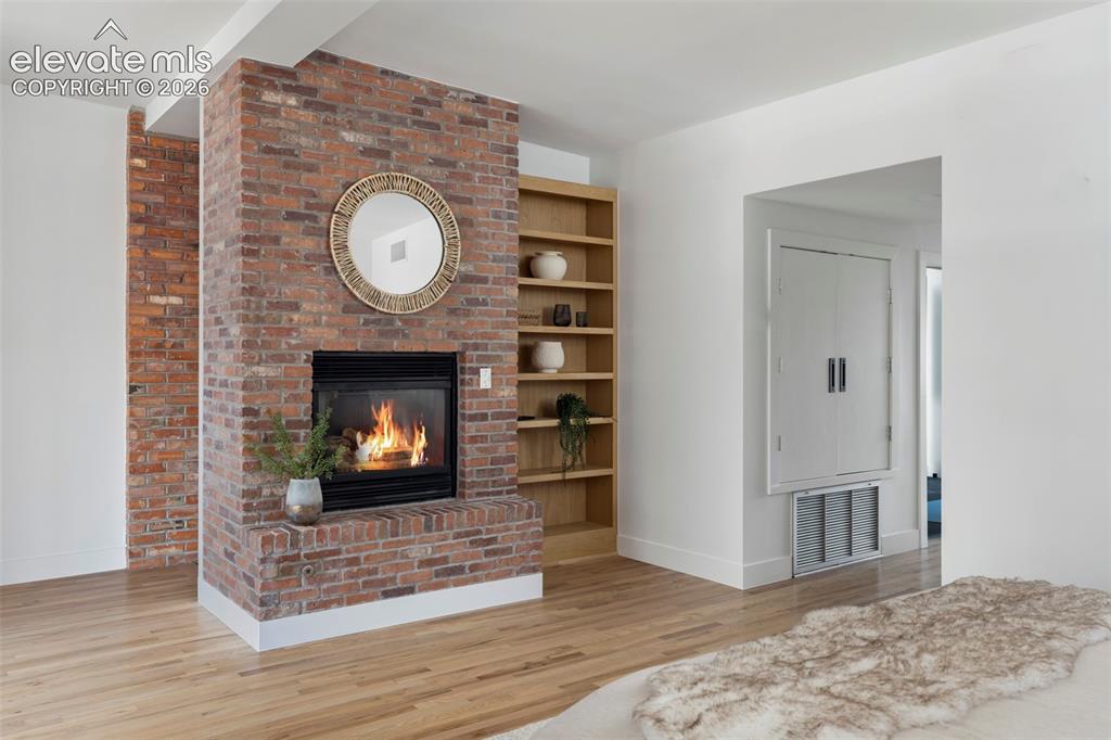 Image 26 of 33: Exposed brick fireplace with a raised hearth, light wood-finish flooring, a