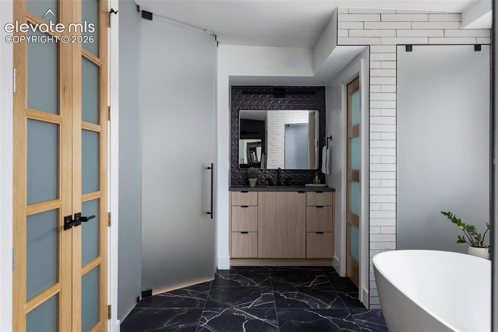 Image 28 of 33: Black marble-look flooring, light wood-finish vanity with dark countertop,
