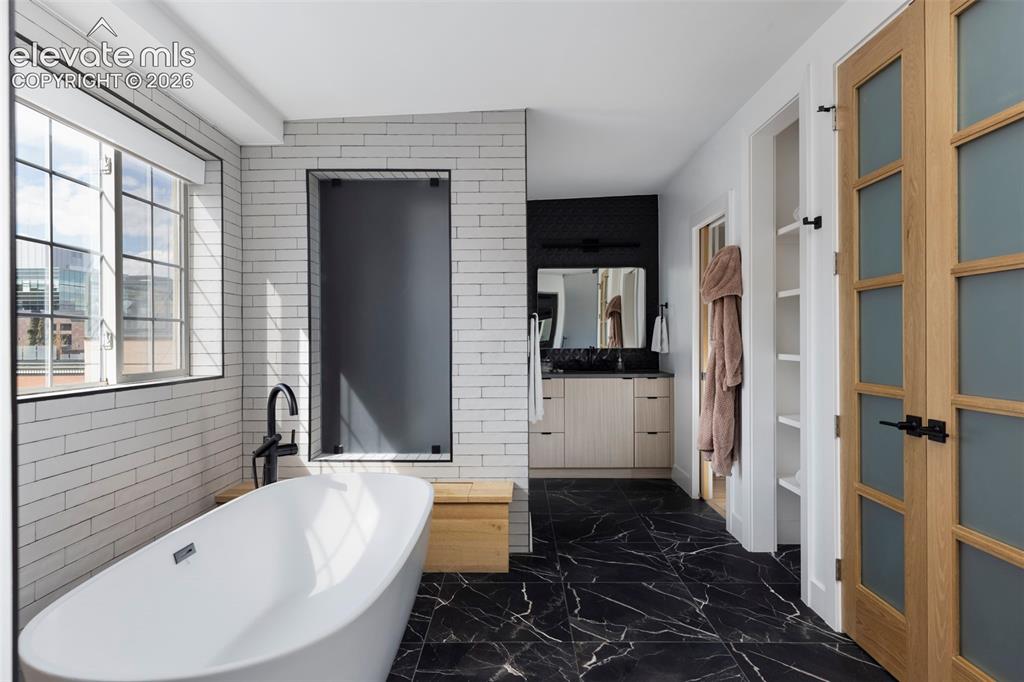 Image 29 of 33: Freestanding soaking tub with floor-mounted faucet, black marble-look tile 