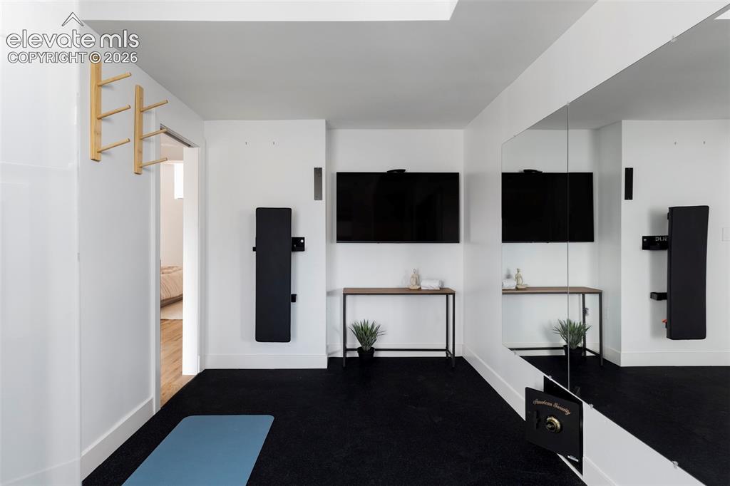 Image 30 of 33: Mirrored wall panel, wall-mounted television, and wood-finish console table