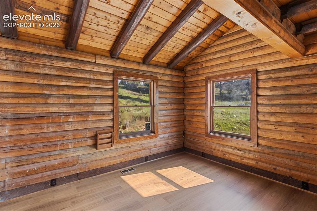 Image 9 of 32: Main level bedroom 1 with new flooring and exposed log walls.