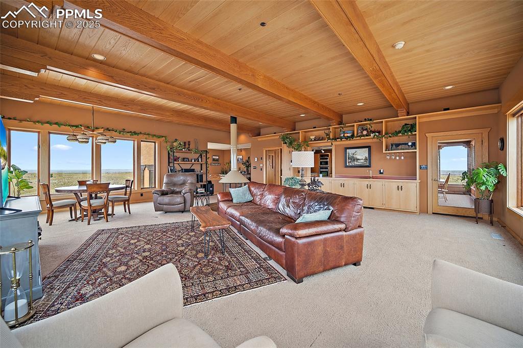 Image 18 of 31: Living area with light colored carpet and a wood ceiling with exposed beams