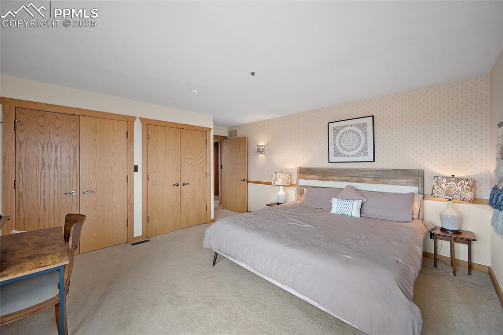 Image 24 of 31: Carpeted bedroom featuring wallpapered walls and two closets