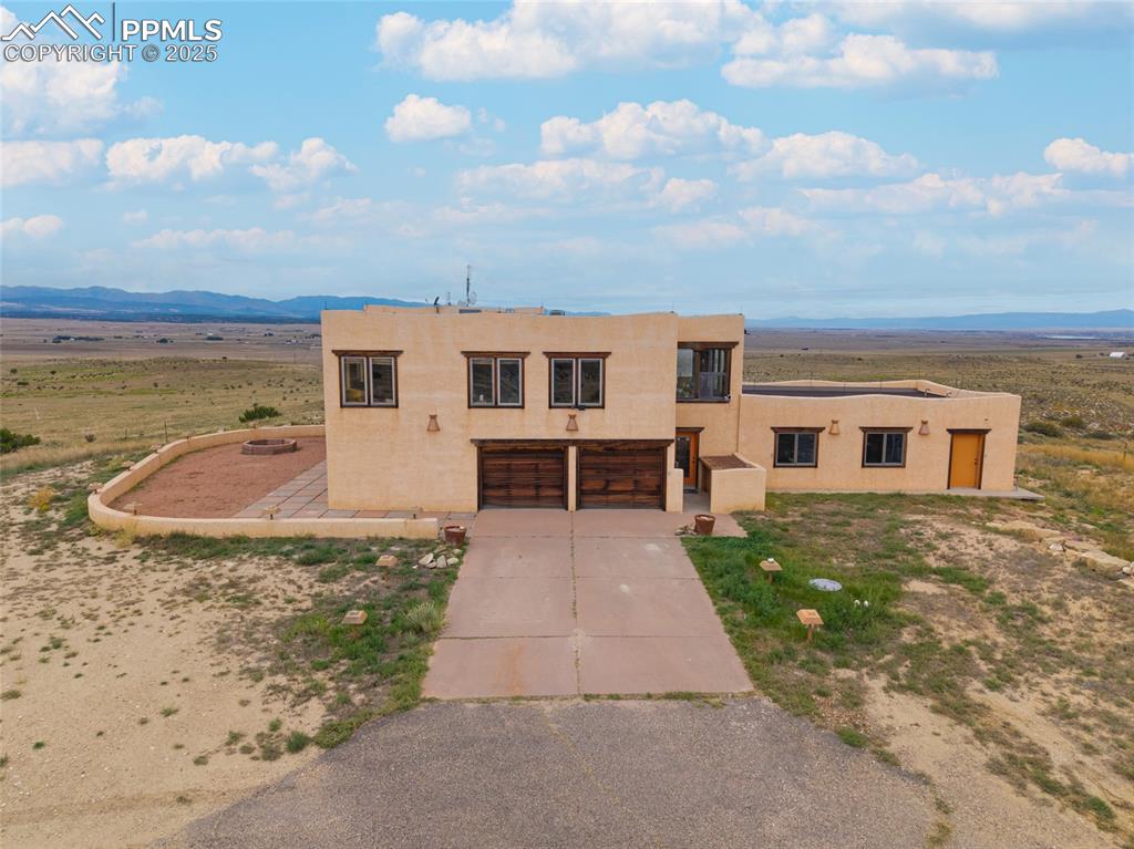 Image 5 of 31: Pueblo revival-style home with stucco siding, concrete driveway, a mountain