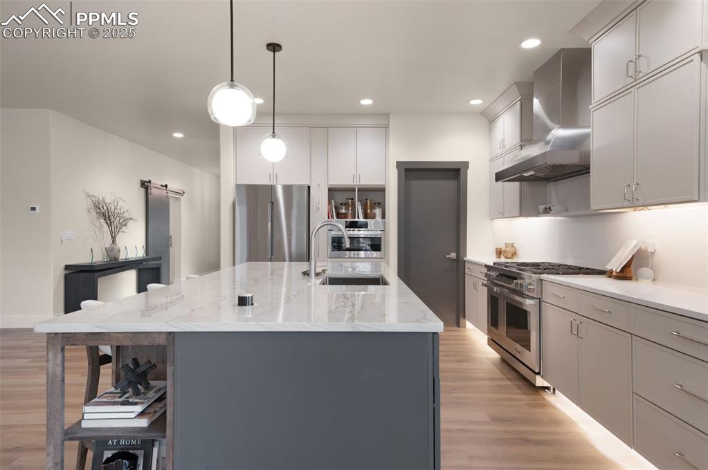 Image 10 of 42: Kitchen with gray cabinetry, a barn door, stainless steel appliances, wall