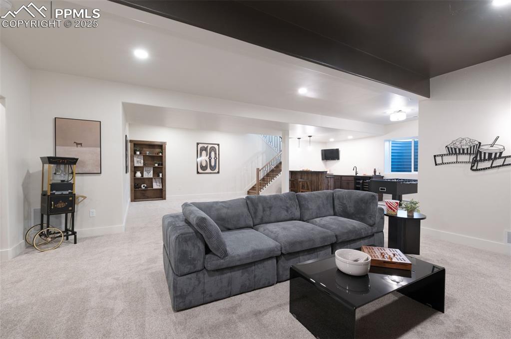 Image 28 of 42: Living area with light colored carpet, stairs, beam ceiling, recessed light
