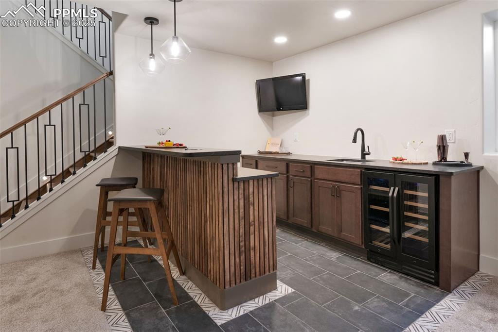 Image 30 of 42: Indoor wet bar featuring dark countertops, wine cooler, hanging light fixtu