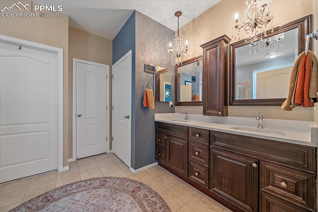 Image 19 of 47: Full bathroom with double vanity, light tile patterned floors, and a chande