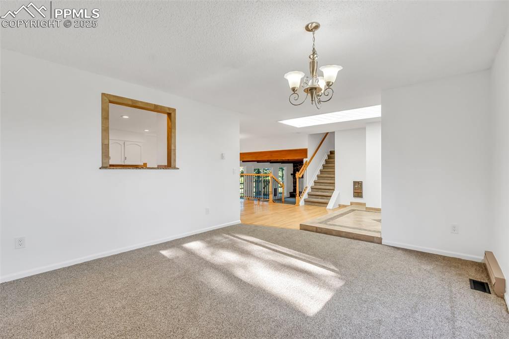 Image 10 of 46: Unfurnished room featuring carpet flooring, stairs, a chandelier, and a tex