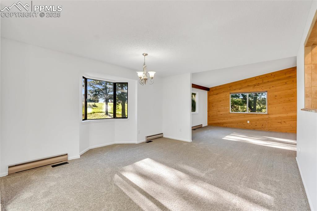 Image 12 of 46: Unfurnished room with wood walls, a chandelier, a baseboard radiator, and c