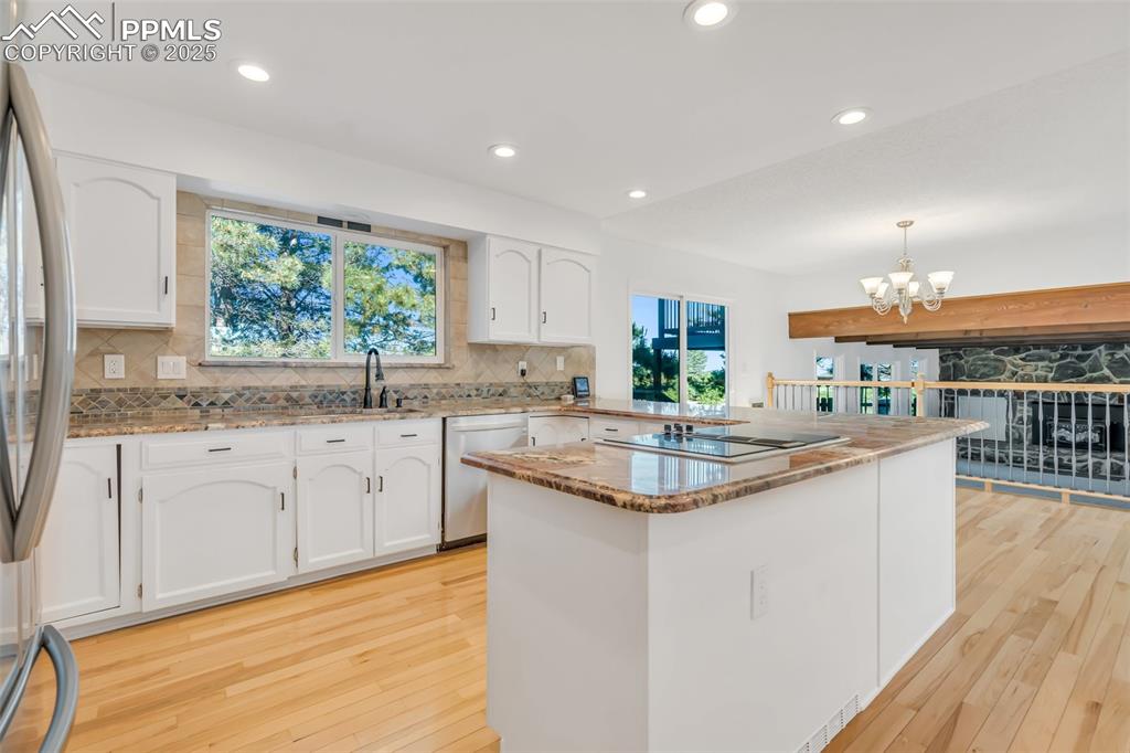 Image 15 of 46: Kitchen with light stone countertops, white cabinets, light wood finished f