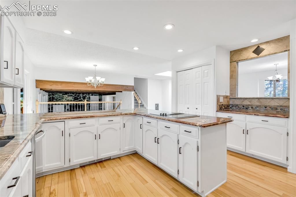 Image 17 of 46: Kitchen with a chandelier, decorative backsplash, white cabinets, light woo