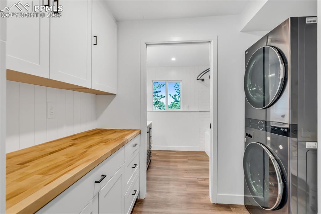 Image 20 of 46: Washroom with estacked washer and dryer, light wood-type flooring, and cabi