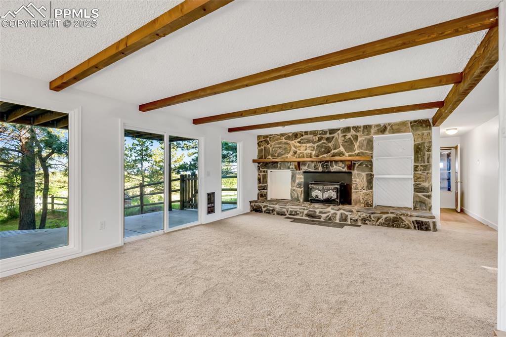 Image 26 of 46: Unfurnished living room with a textured ceiling, carpet flooring, a stone f
