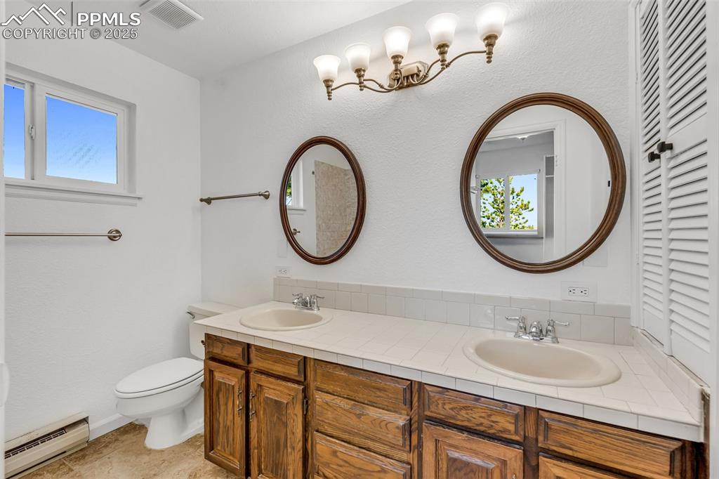 Image 32 of 46: Bathroom featuring a baseboard radiator, double vanity, and plenty of natur