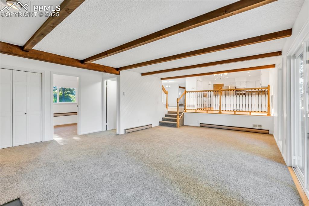 Image 4 of 46: Unfurnished living room with beam ceiling, carpet flooring, stairs, a baseb