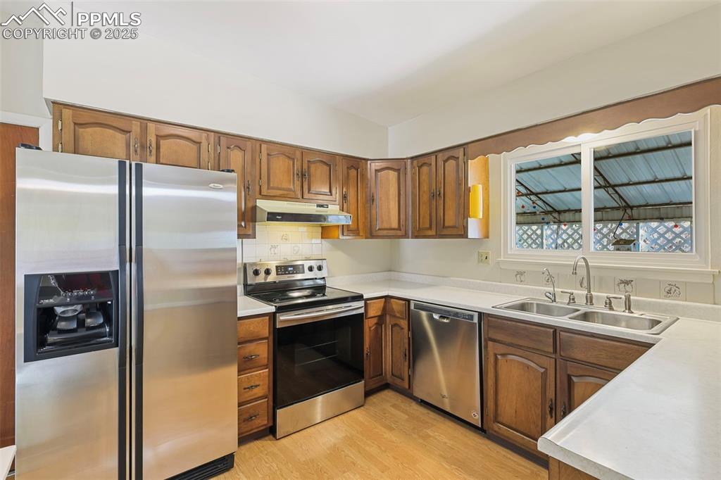 Image 7 of 35: Kitchen featuring stainless steel appliances, brown cabinetry, and light co