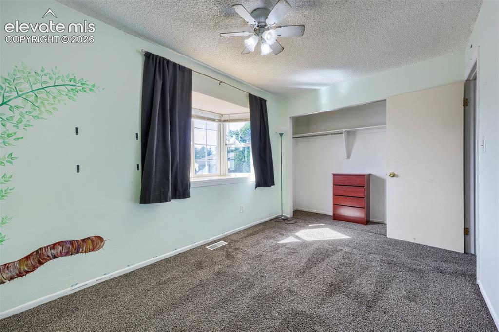 Image 28 of 38: Carpeted room featuring a bay window, ceiling fan, and built-in closet with