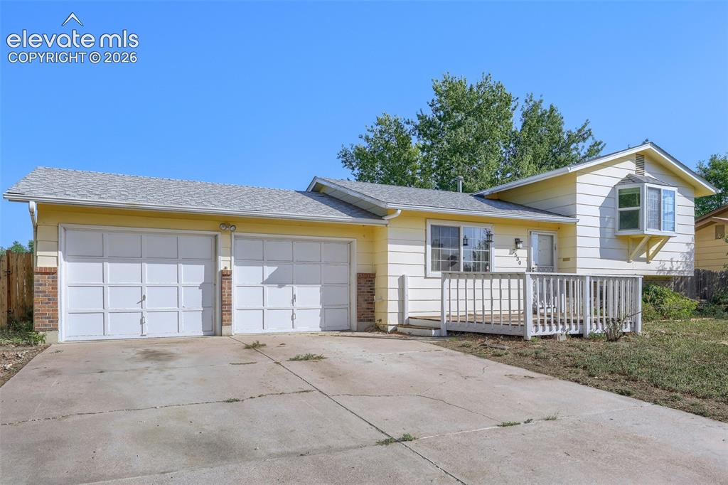 Image 3 of 38: Yellow siding exterior with a two-car garage, front entry deck, and a bay w