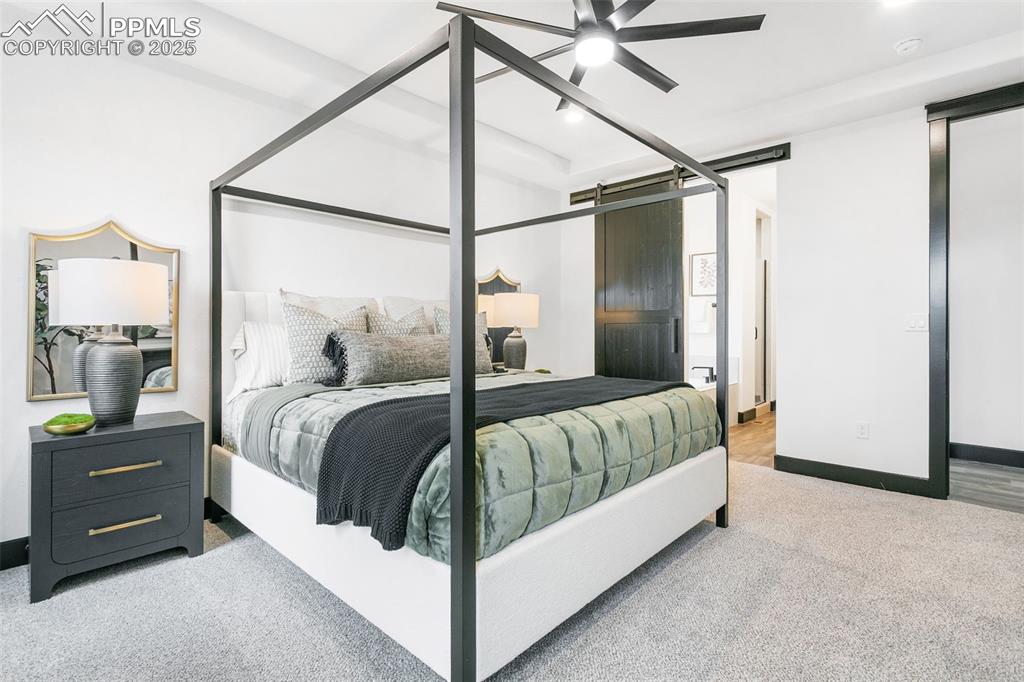 Image 15 of 22: Bedroom with a barn door, light colored carpet, and ceiling fan