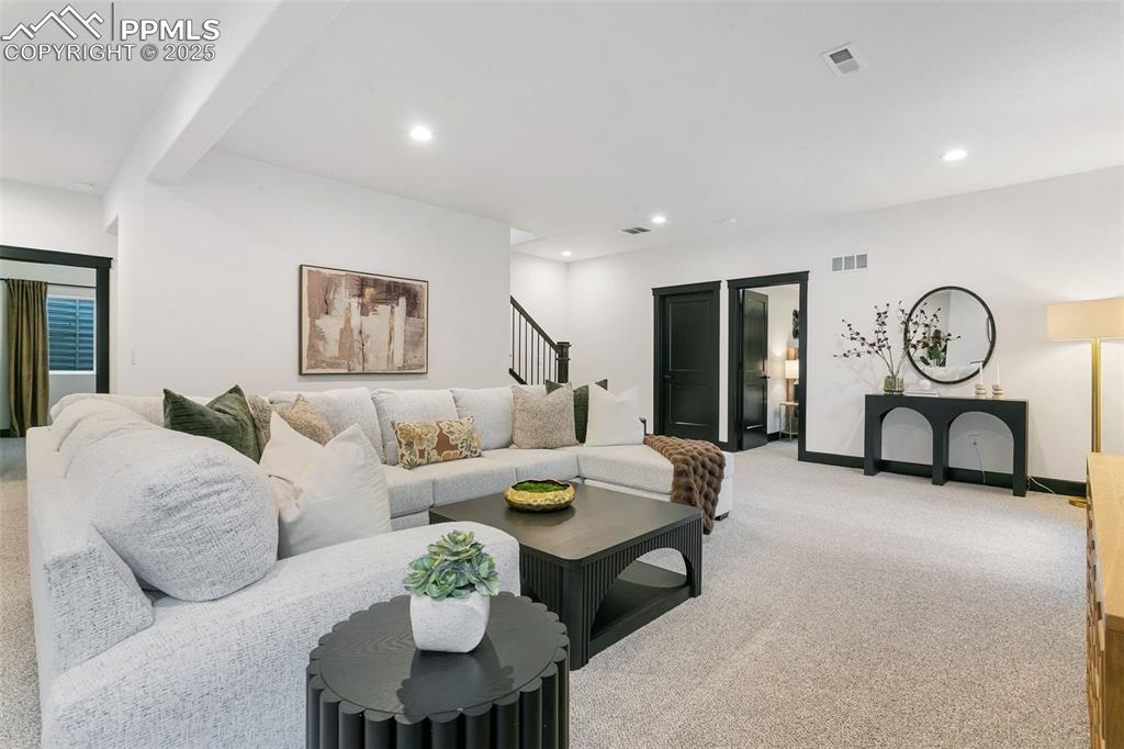 Image 17 of 22: Living room with light colored carpet, recessed lighting, and stairs