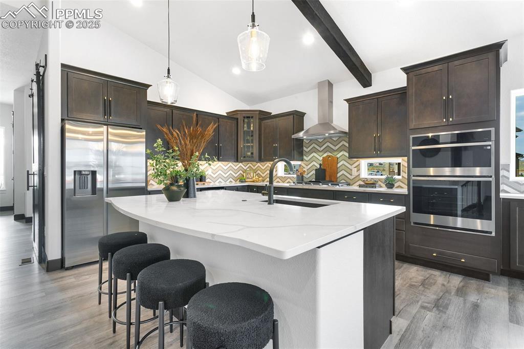 Image 6 of 22: Kitchen with tasteful backsplash, dark brown cabinetry, a center island wit