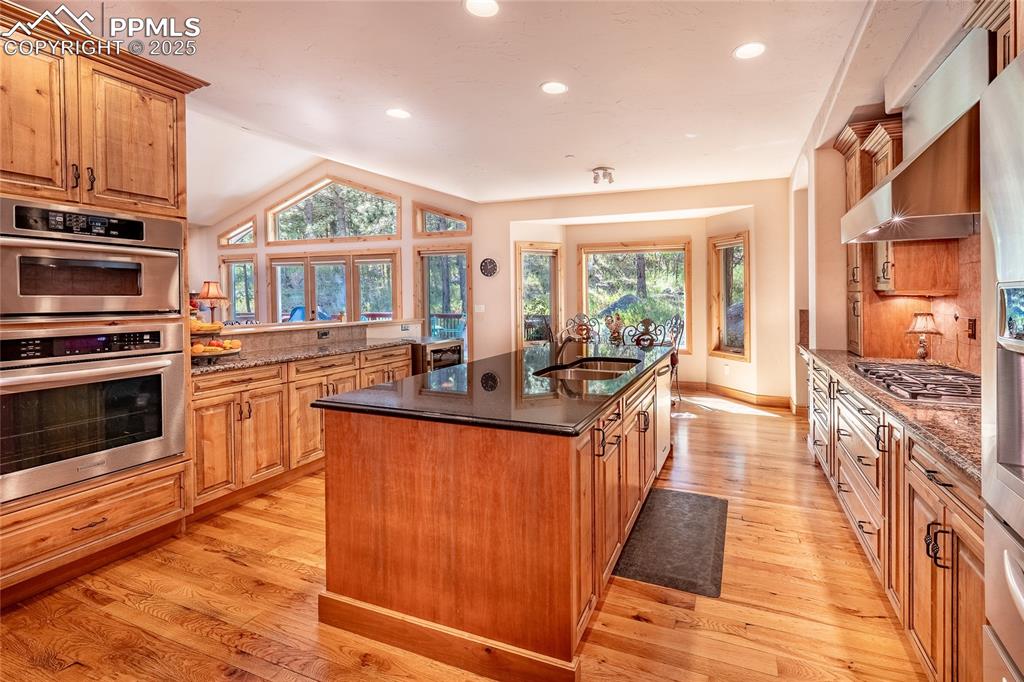 Image 12 of 47: Kitchen with an island with sink, tasteful backsplash, brown cabinetry, rec