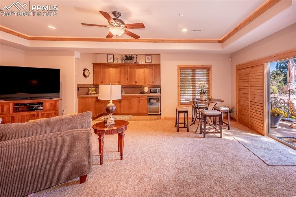Image 13 of 47: Family room with a raised ceiling, light carpet, a ceiling fan, beverage co
