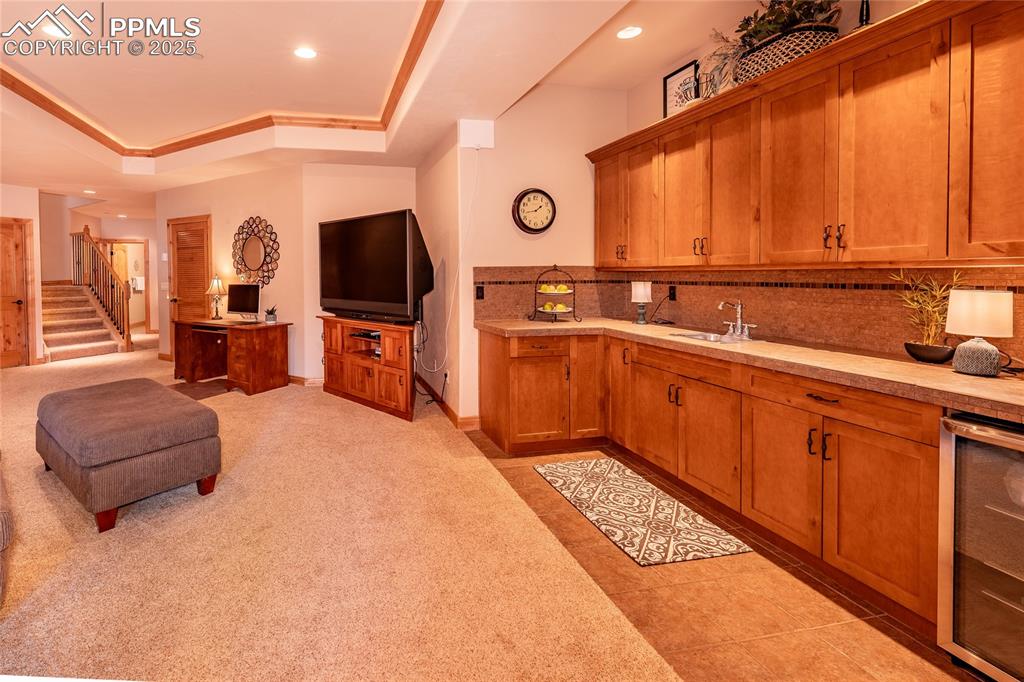 Image 14 of 47: Wet bar with beverage cooler, a tray ceiling, tasteful backsplash, open flo