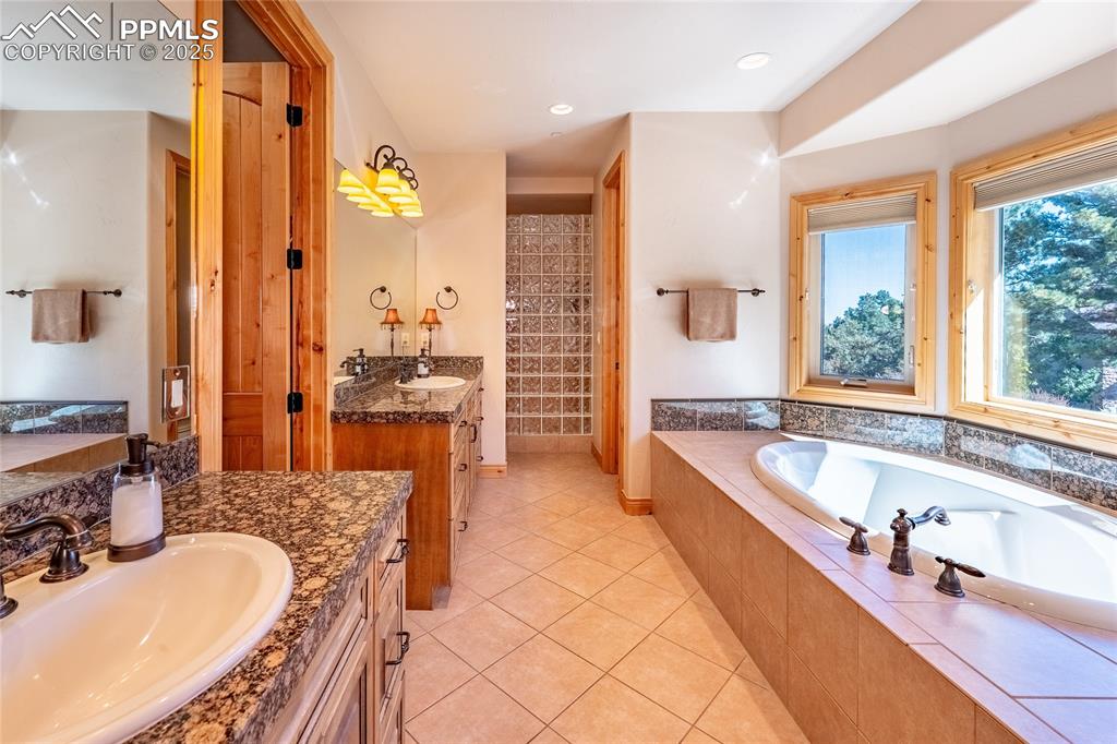 Image 18 of 47: Full bathroom with two vanities, a bath, light tile patterned floors, walk