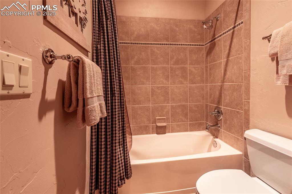 Image 30 of 47: Bathroom featuring a textured wall and shower / tub combo with curtain