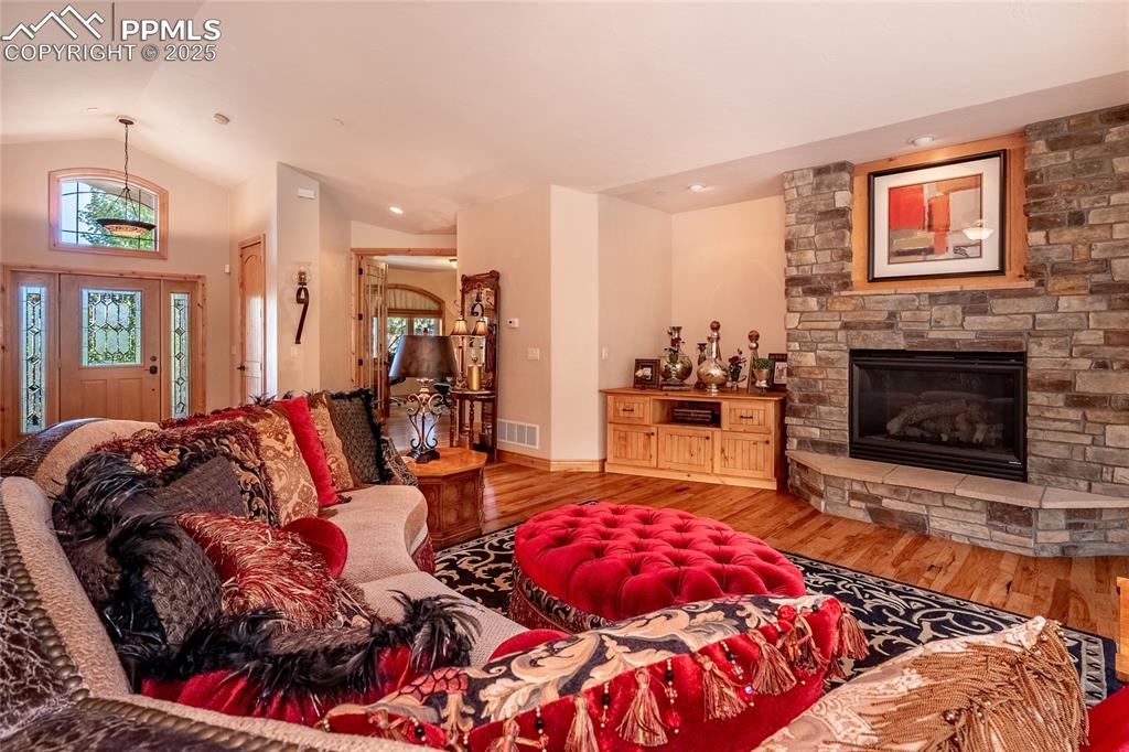 Image 8 of 47: Living room with wood finished floors, vaulted ceiling, and a fireplace