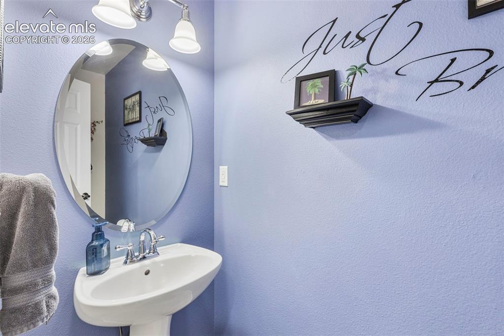 Image 10 of 28: Pedestal sink with chrome faucet, oval mirror, and wall-mounted light fixtu