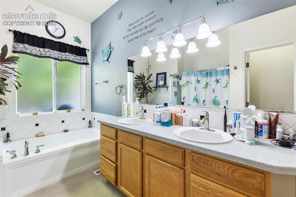 Image 14 of 28: Double vanity with wood-finish cabinetry, built-in bathtub, window with pri