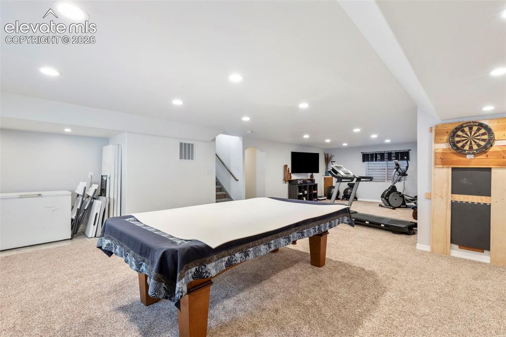 Image 21 of 28: Expansive carpeted area with recessed lighting, a dartboard wall feature, a