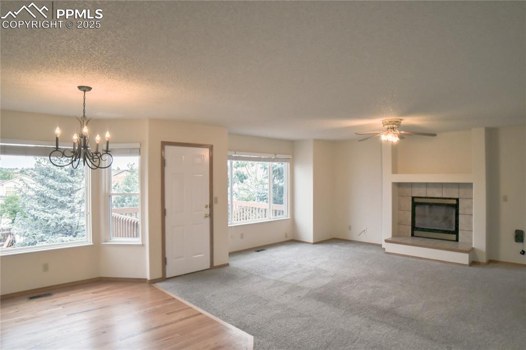Image 15 of 48: Unfurnished living room with a chandelier, a ceiling fan, a tiled fireplace