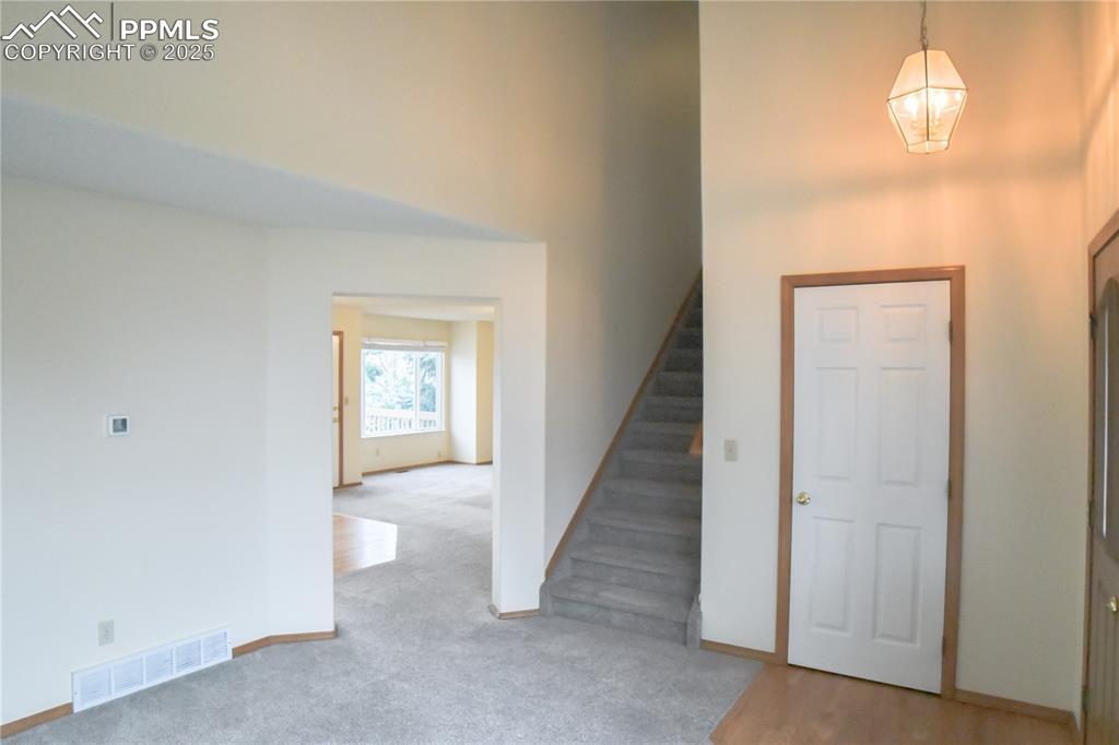 Image 24 of 48: Entrance foyer with light colored carpet, a high ceiling, stairway, and a c